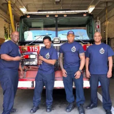 Four men in blue shirts standing next to a fire truck.